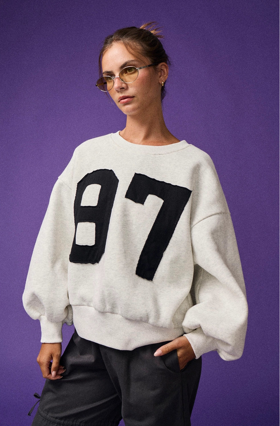 Person wearing a white sweater with black numbers against a purple background