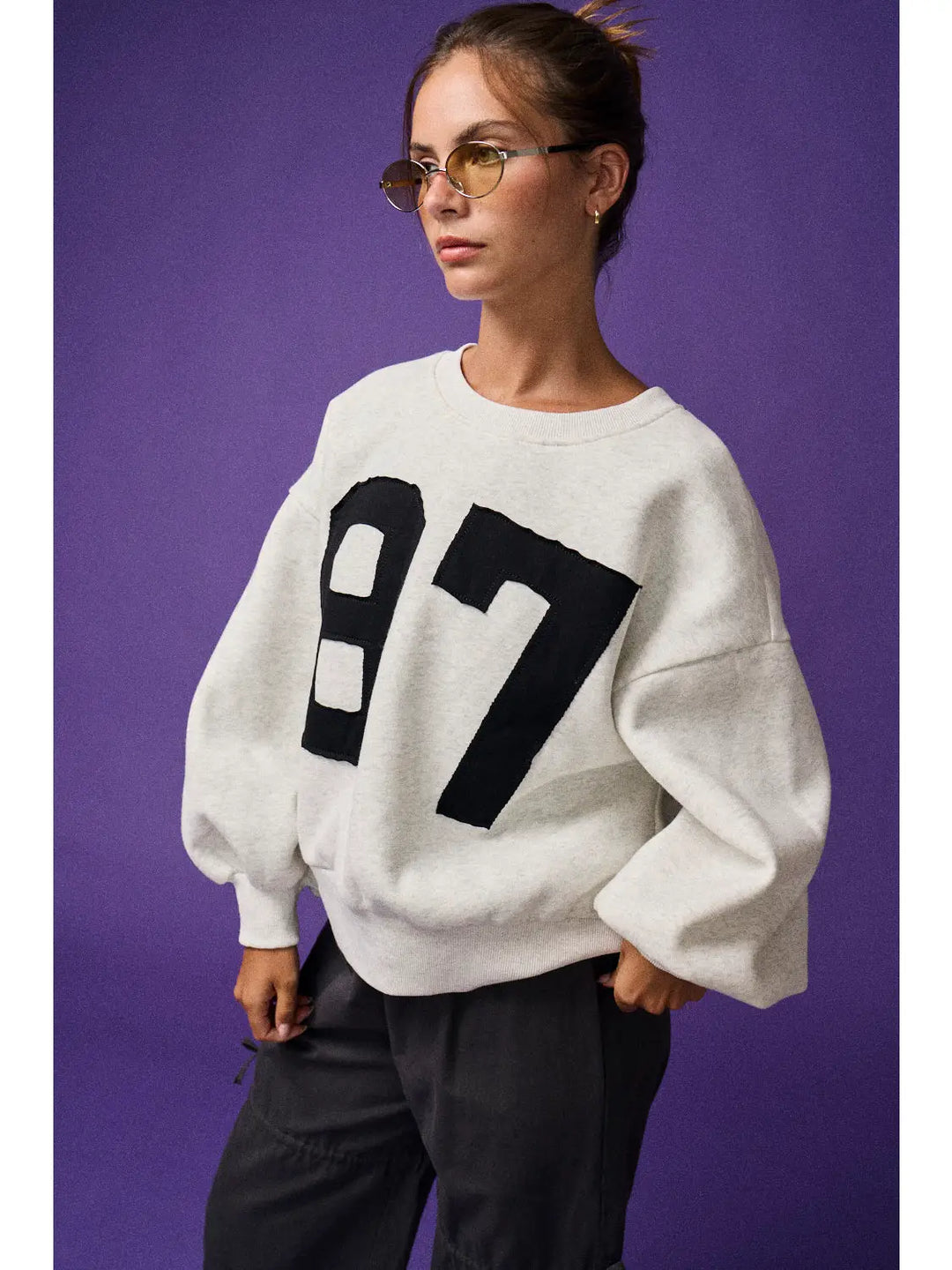 Person wearing a white sweater with black numbers on a purple background