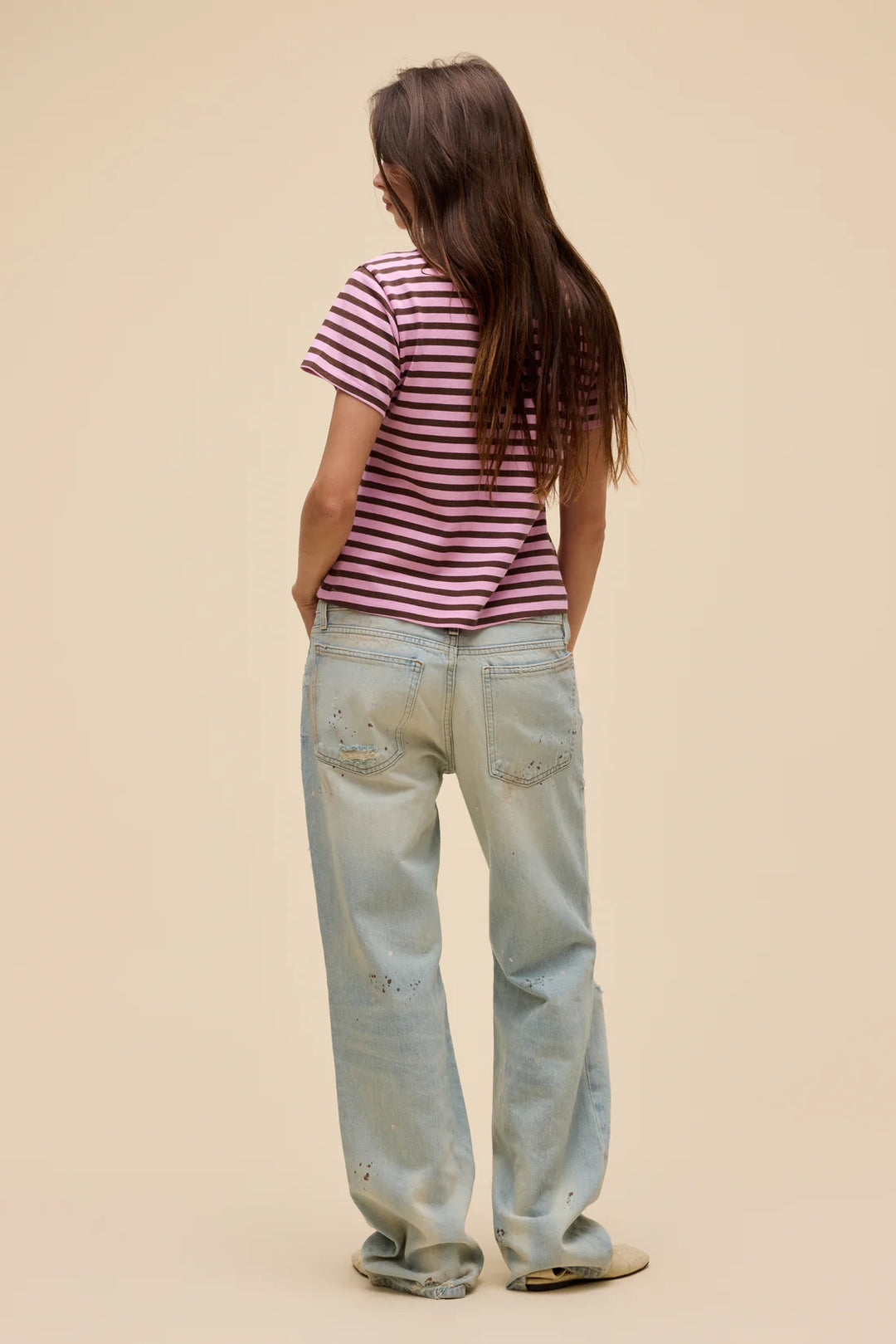 Person wearing a striped shirt and light blue jeans on a beige background