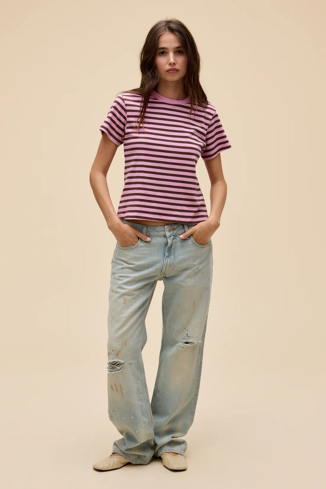 Woman wearing a striped shirt and light blue jeans against a beige background