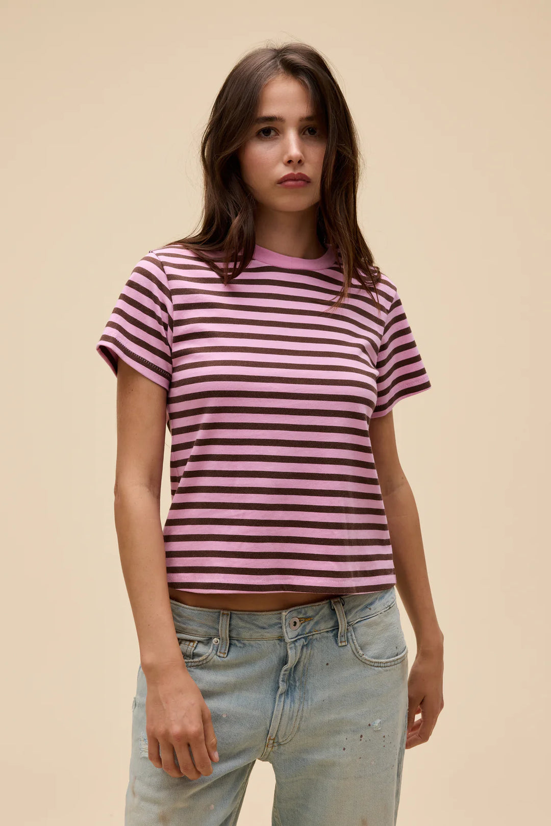 Woman wearing a pink and purple striped shirt with light blue jeans against a beige background