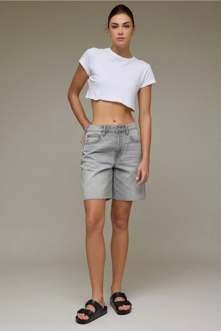 Woman wearing a white crop top and gray shorts against a plain background