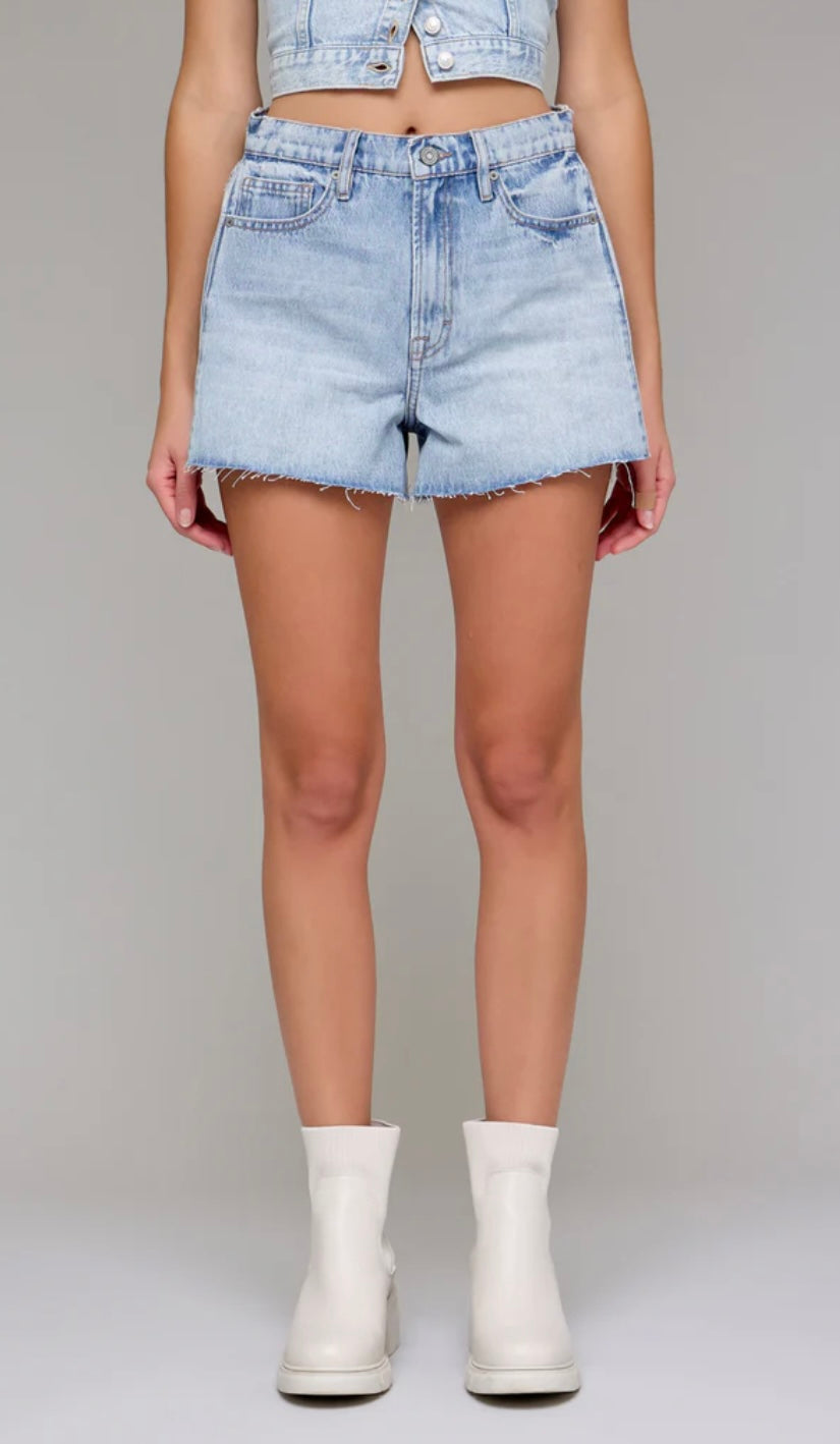 Person wearing light blue denim shorts and white boots on a plain background