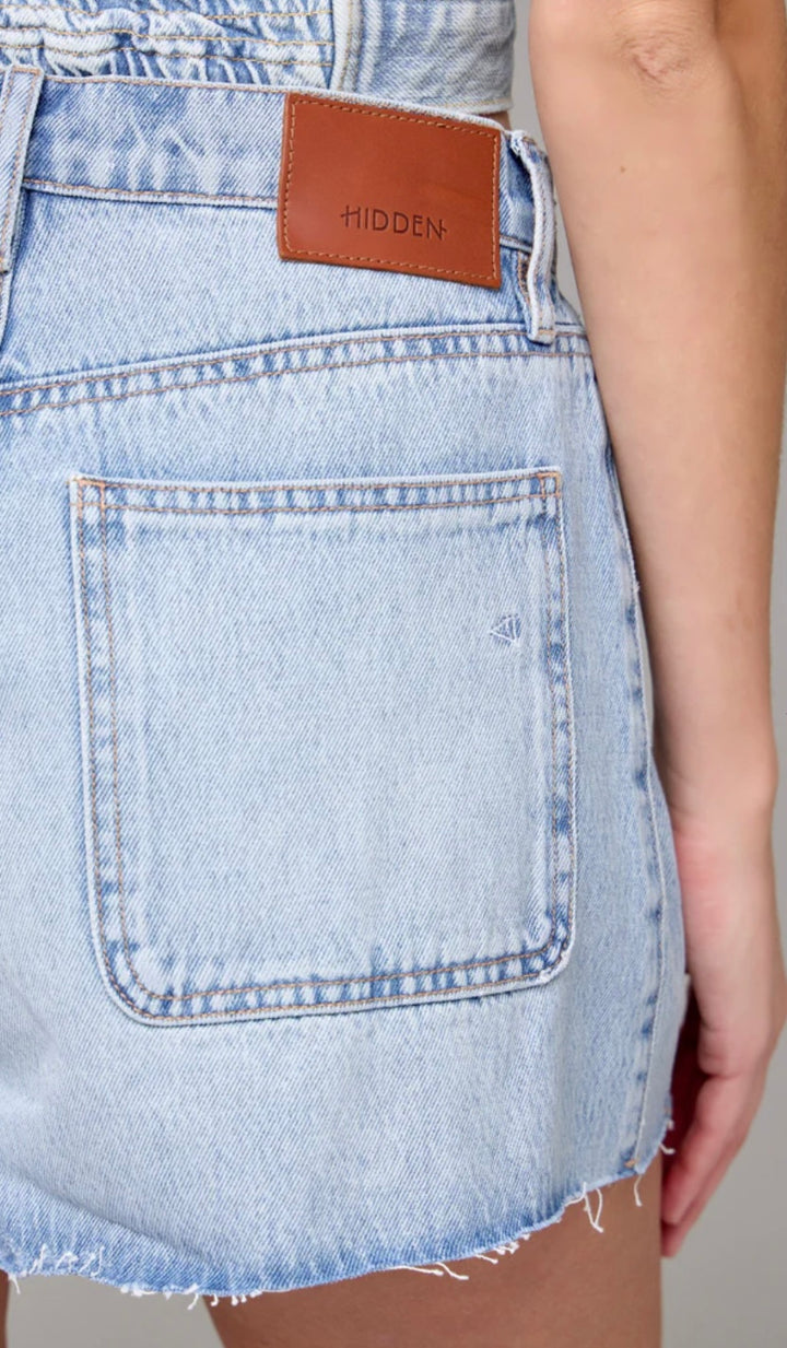 Light blue denim skirt with a brown label on a neutral background