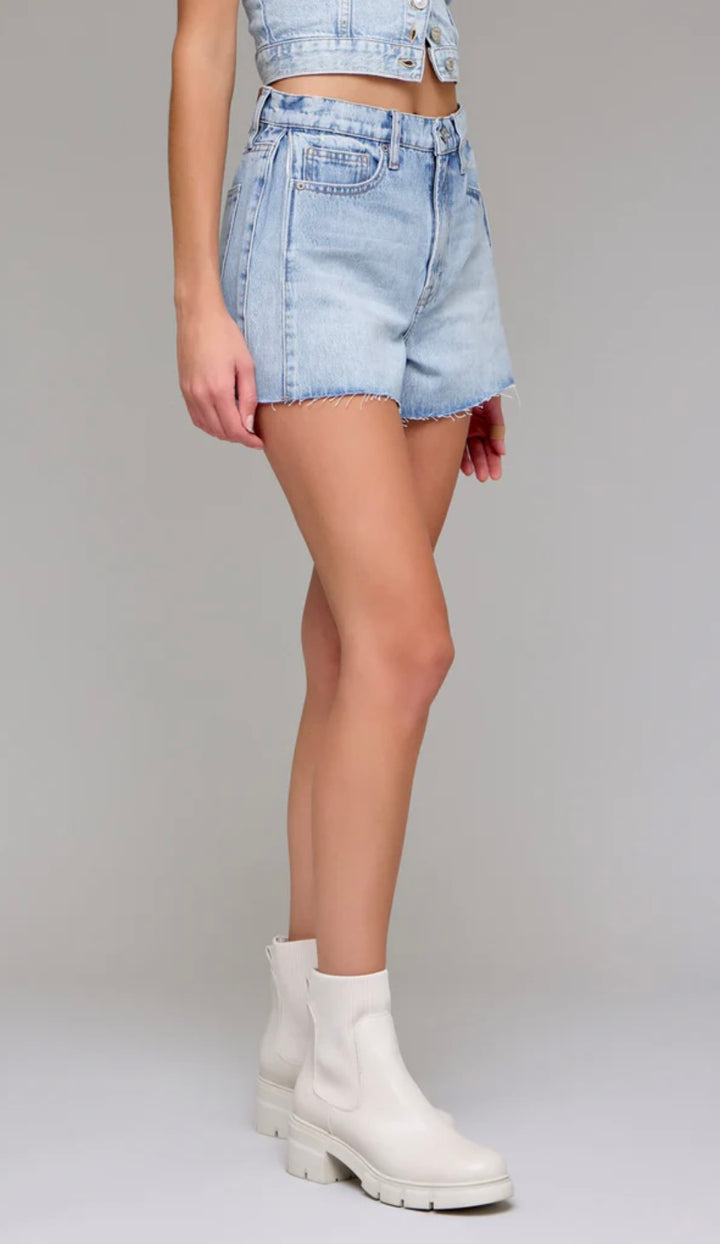 Person wearing light blue denim shorts and white boots on a plain background