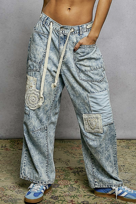 Person wearing light blue acid-wash jeans with patches on a patterned rug.