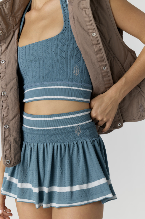 Woman wearing a blue knit top and skirt with a brown jacket on a white background
