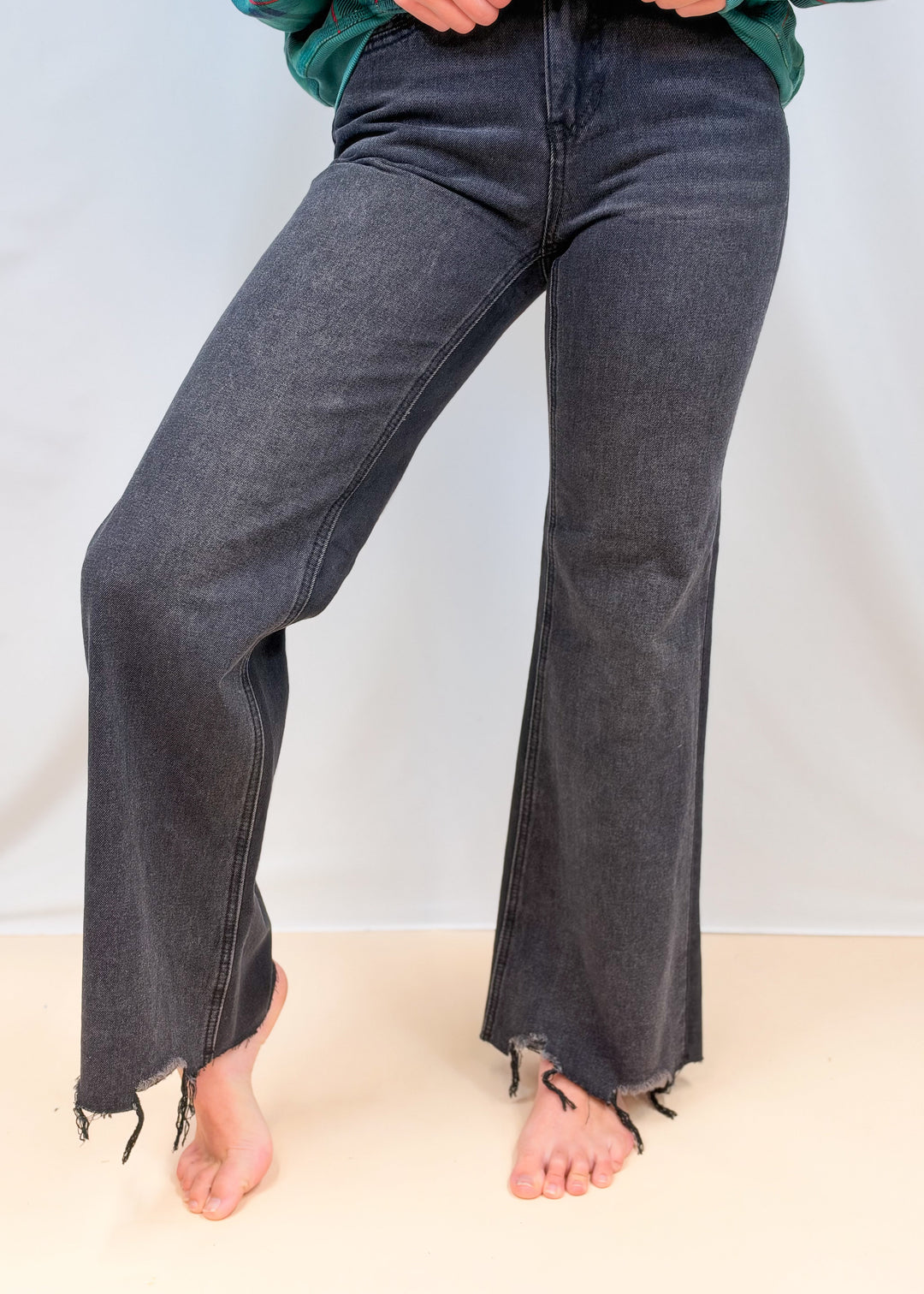 Woman shown from waist down wearing black flare jeans on plain background
