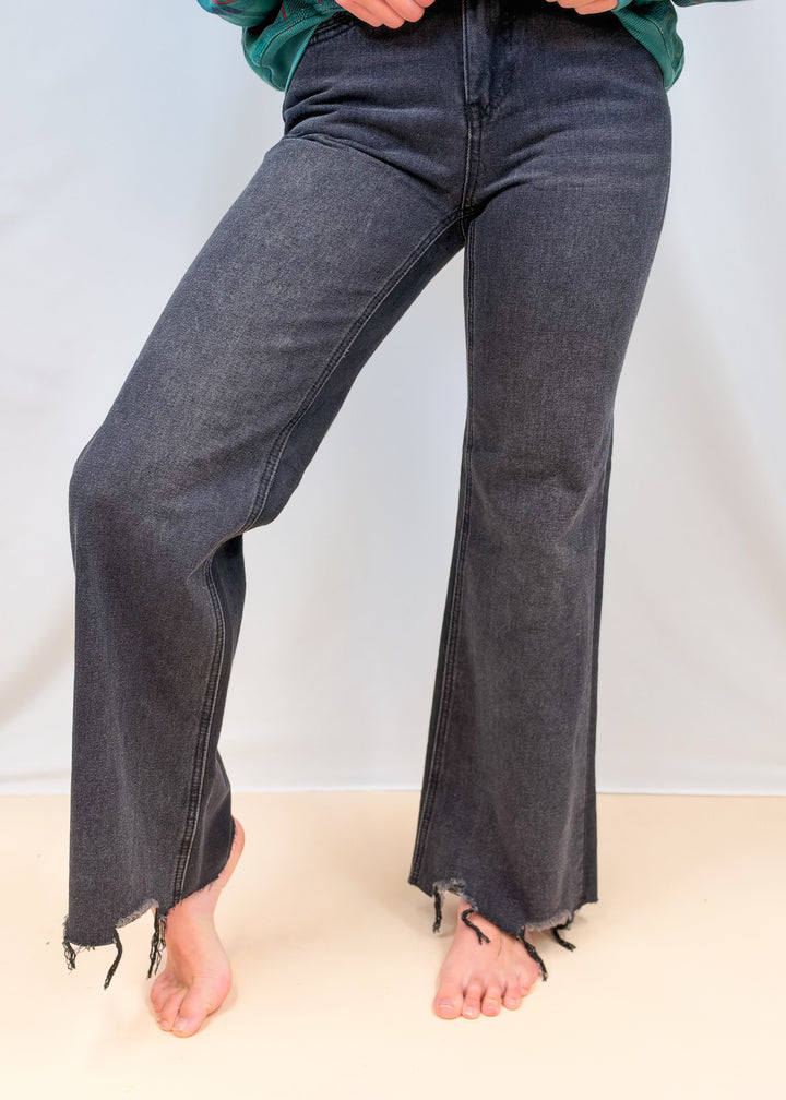 Woman shown from waist down wearing black flare jeans on plain background