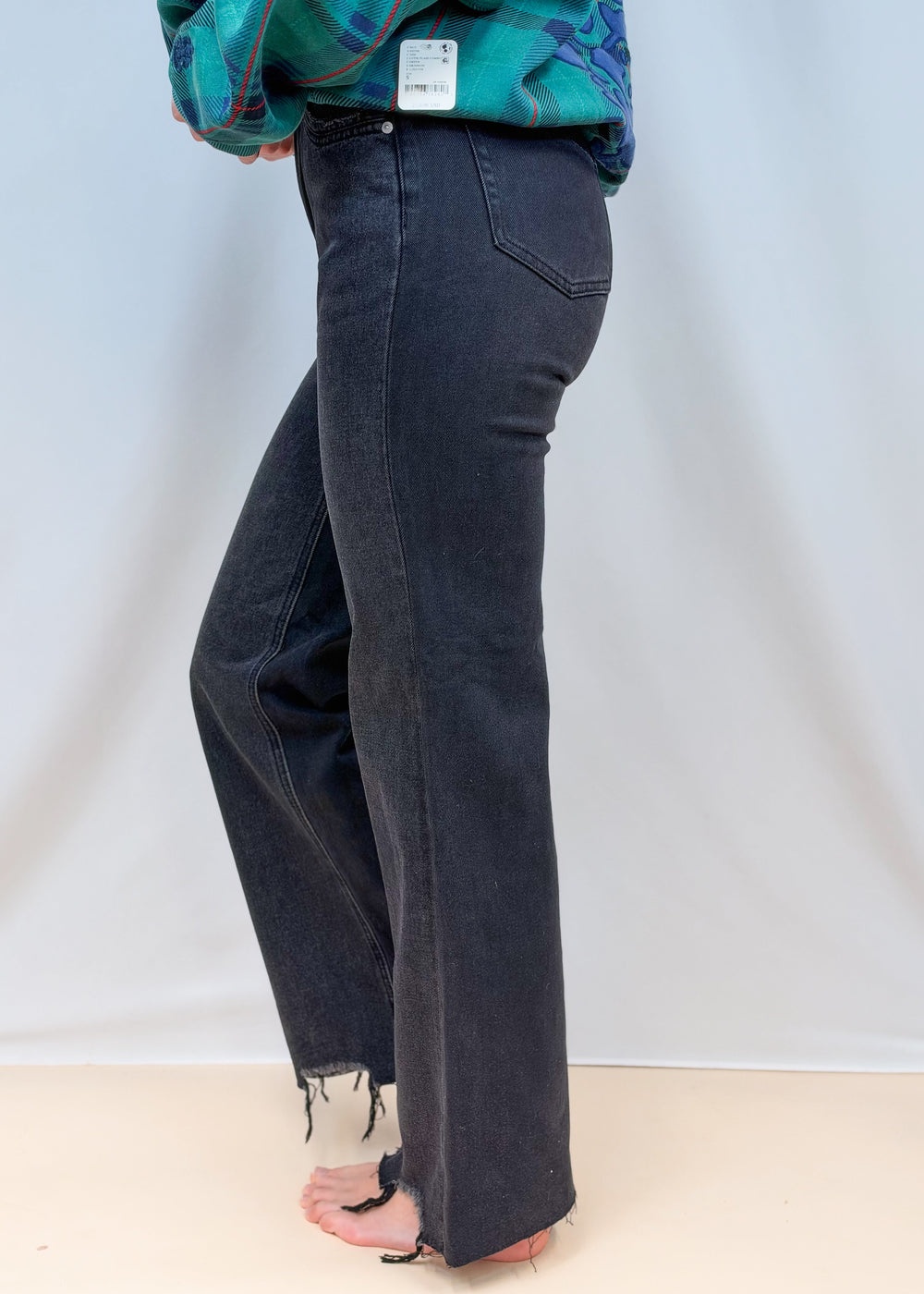 Woman shown from side view waist down wearing black flare denim jeans on plain background