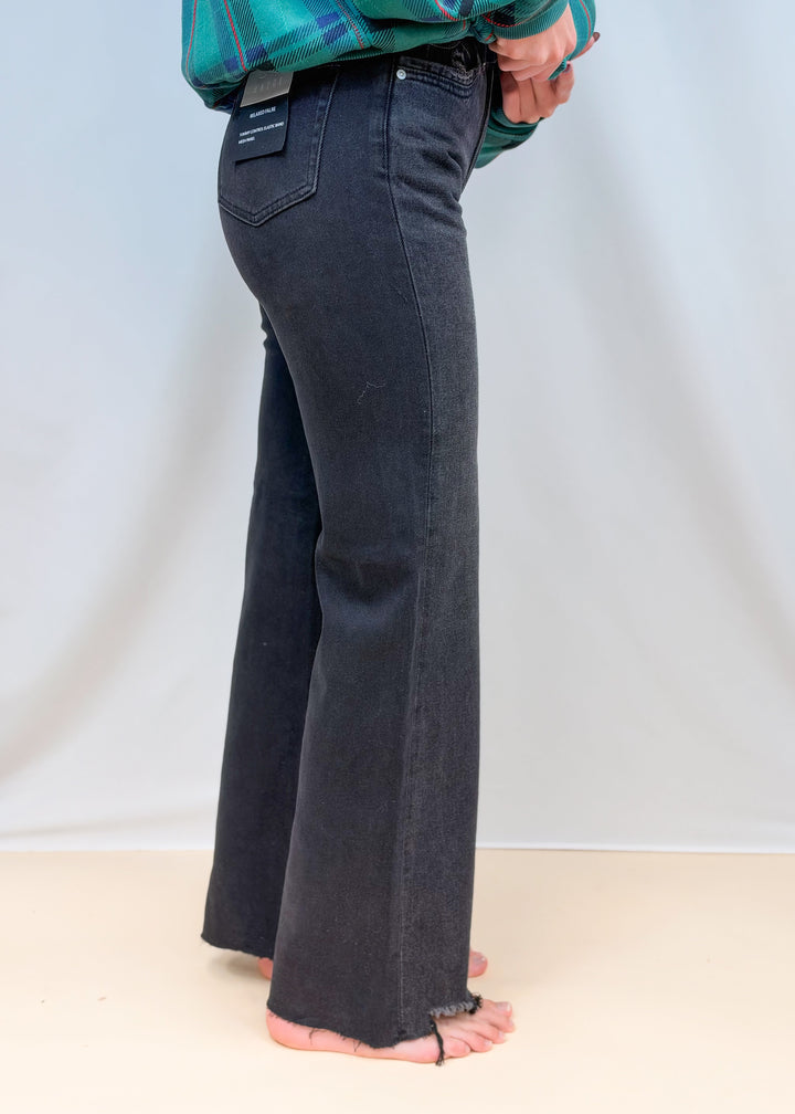 Woman shown from side view waist down wearing black denim flare jeans on plain background