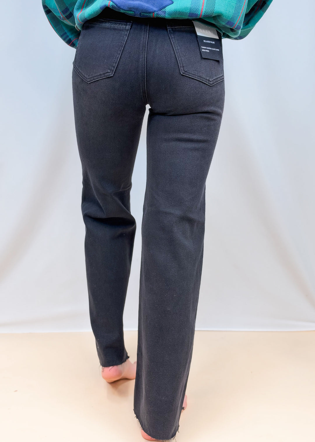 Woman shown from back view waist down wearing black denim flare jeans on plain background