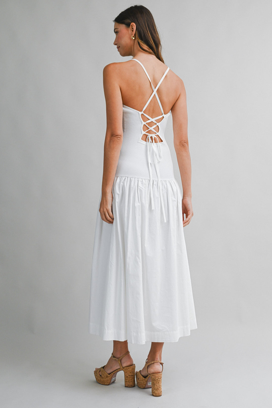 Woman wearing a white dress with criss-cross straps on a plain background