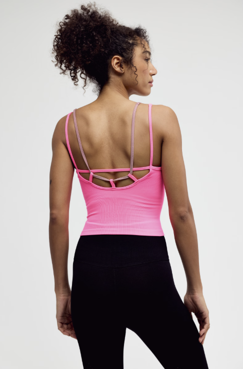 Woman wearing a pink strappy top and black pants on a white background