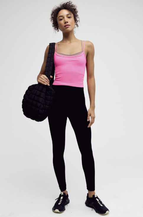 Woman in pink tank top and black leggings holding a black bag on a white background