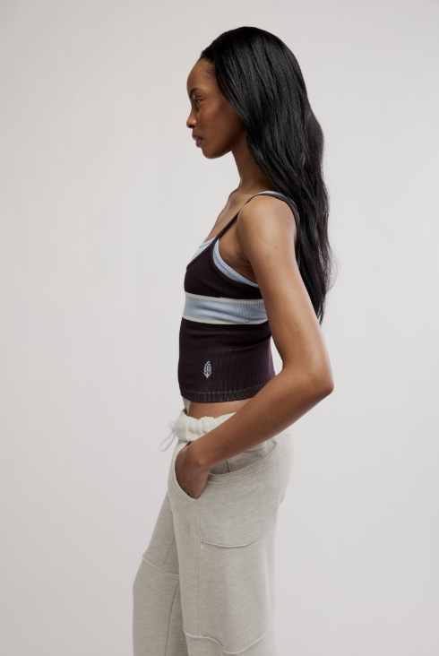 A woman in side profile wearing a dark brown ribbed knit crop top with light blue horizontal stripes and white drawstring sweatpants, photographed against a plain light gray studio background.