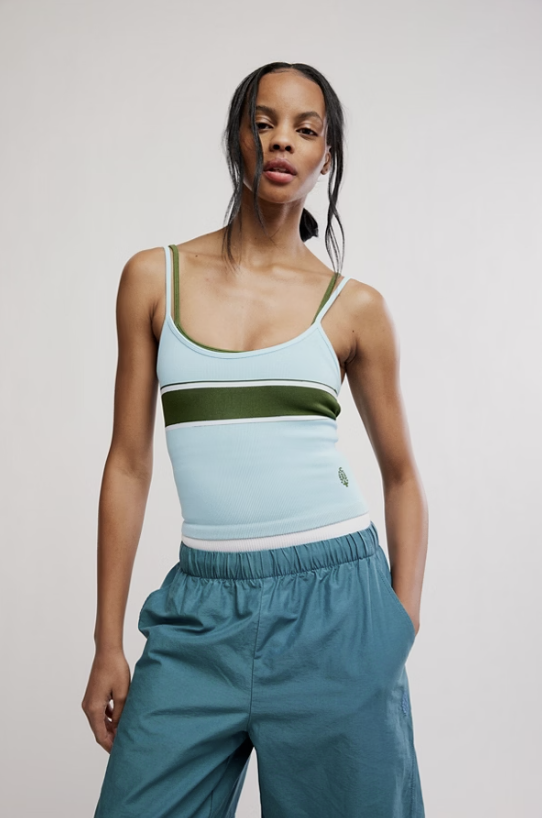 A model wearing a light blue tank top with olive green and white horizontal stripes, paired with teal wide-leg pants, against a plain light gray studio background.