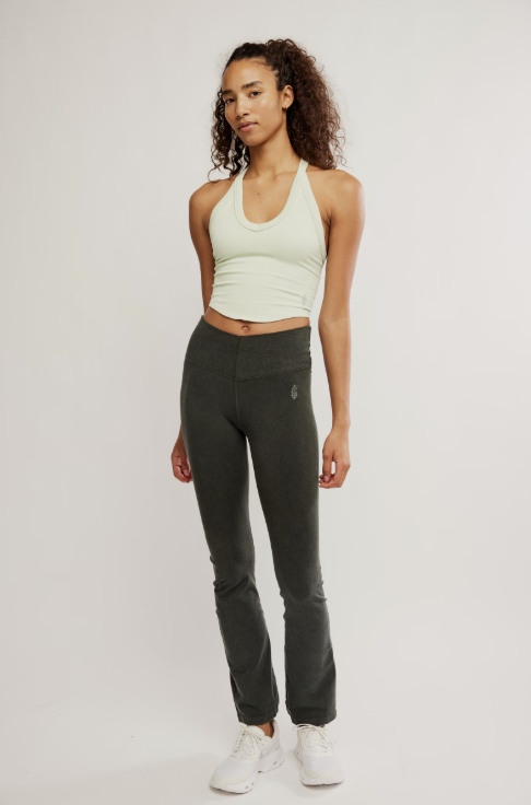 Woman wearing a light green sports bra and dark green leggings on a white background