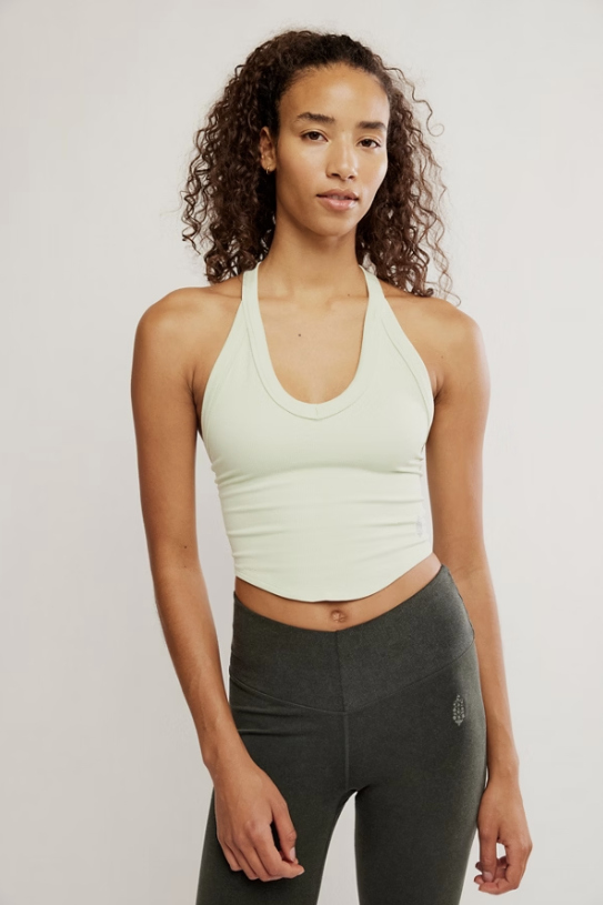 Woman wearing a light green sports bra and dark gray leggings on a plain background