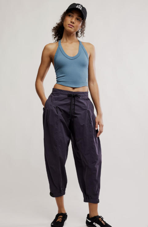Woman wearing a blue tank top and purple pants against a white background