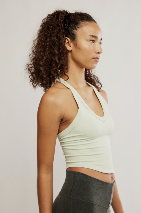 Woman wearing a light green tank top and dark gray leggings against a plain background
