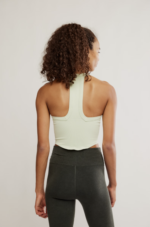 Person wearing a light green tank top and dark gray leggings on a plain background