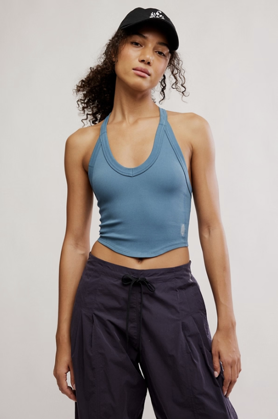 Woman wearing a blue tank top and dark pants against a plain background