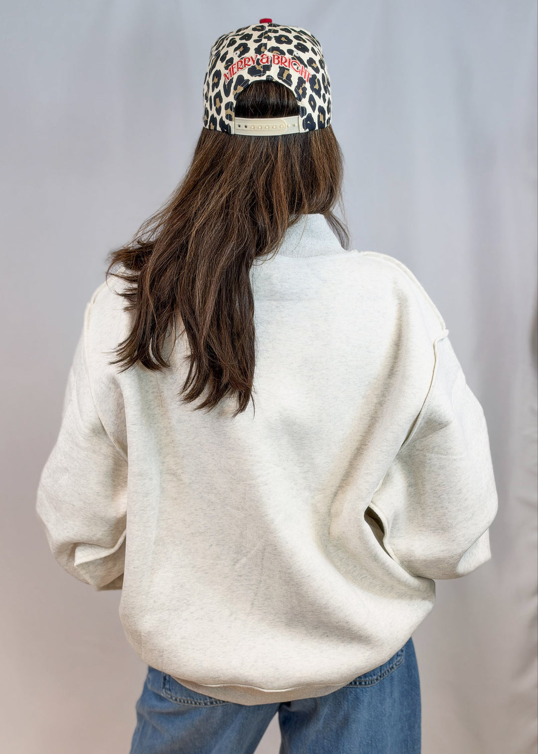 Woman shown from back wearing grey mock neck sweatshirt and jeans on plain background