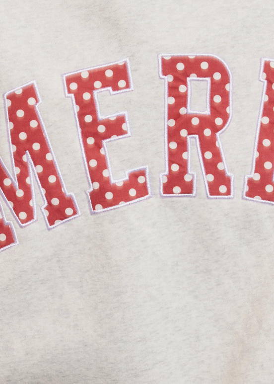 Close-up of a light heather gray sweatshirt featuring large red varsity-style letters with white polka dots and a white stitched border.