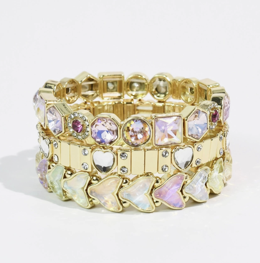 A gold-tone stretch bracelet featuring a mix of iridescent rhinestones, clear crystal hearts, and butterfly-shaped stones, displayed on a clean white background.