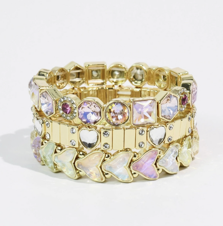A gold-tone stretch bracelet featuring a mix of iridescent rhinestones, clear crystal hearts, and butterfly-shaped stones, displayed on a clean white background.