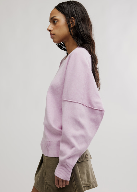 Woman shown from the side wearing light purple pullover and olive skirt on plain background