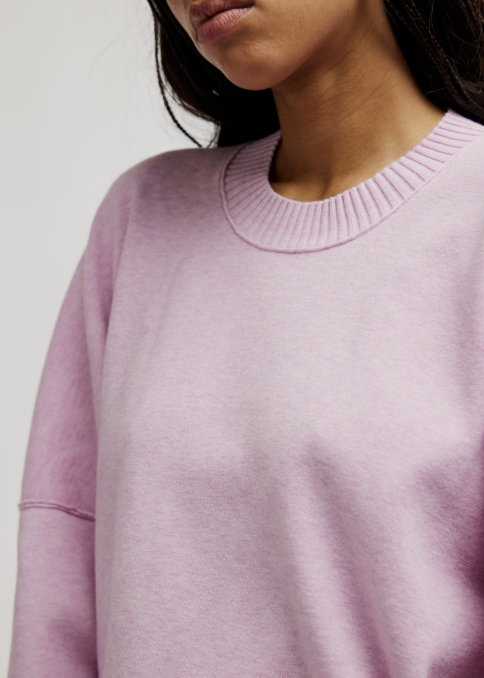 Close up of woman wearing light purple pullover on plain background