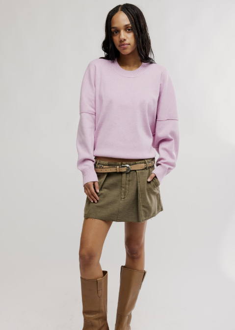 Woman wearing light purple pullover and olive skirt with knee high boots on plain background