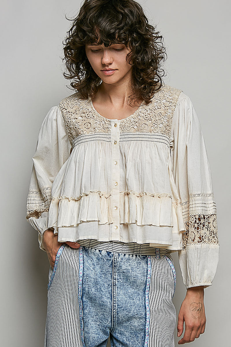 Woman wearing a white lace blouse with long sleeves and blue jeans against a plain background