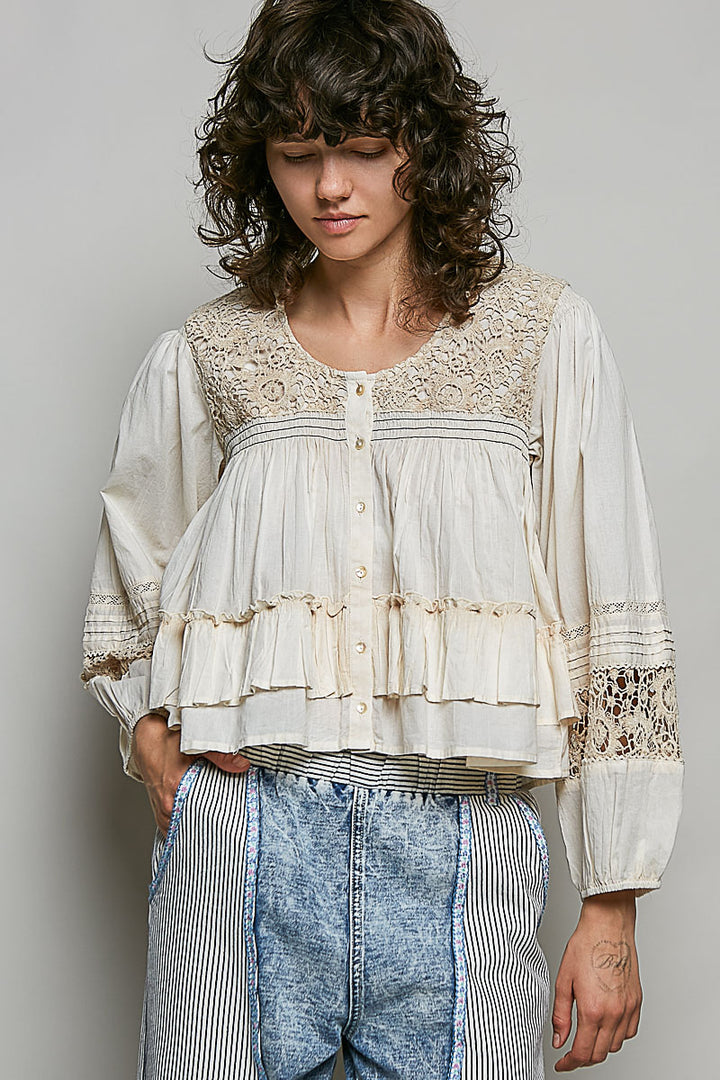 Woman wearing a white lace blouse with long sleeves and blue jeans against a plain background