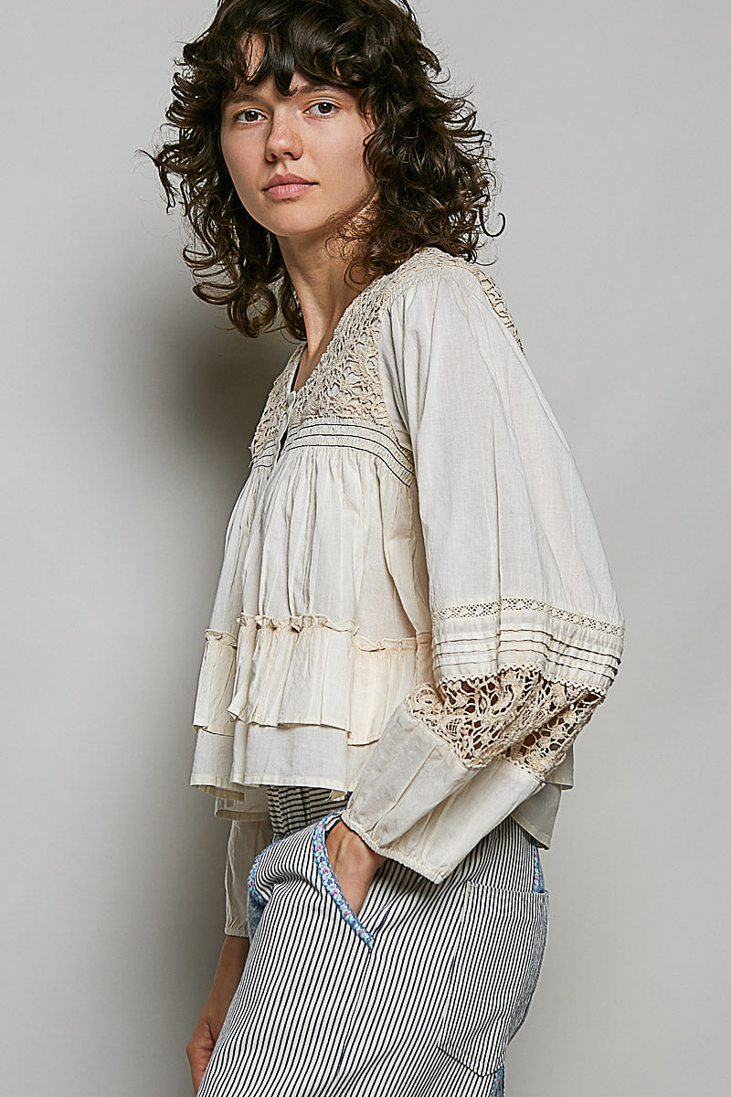Person wearing a light-colored blouse with lace details on a plain background