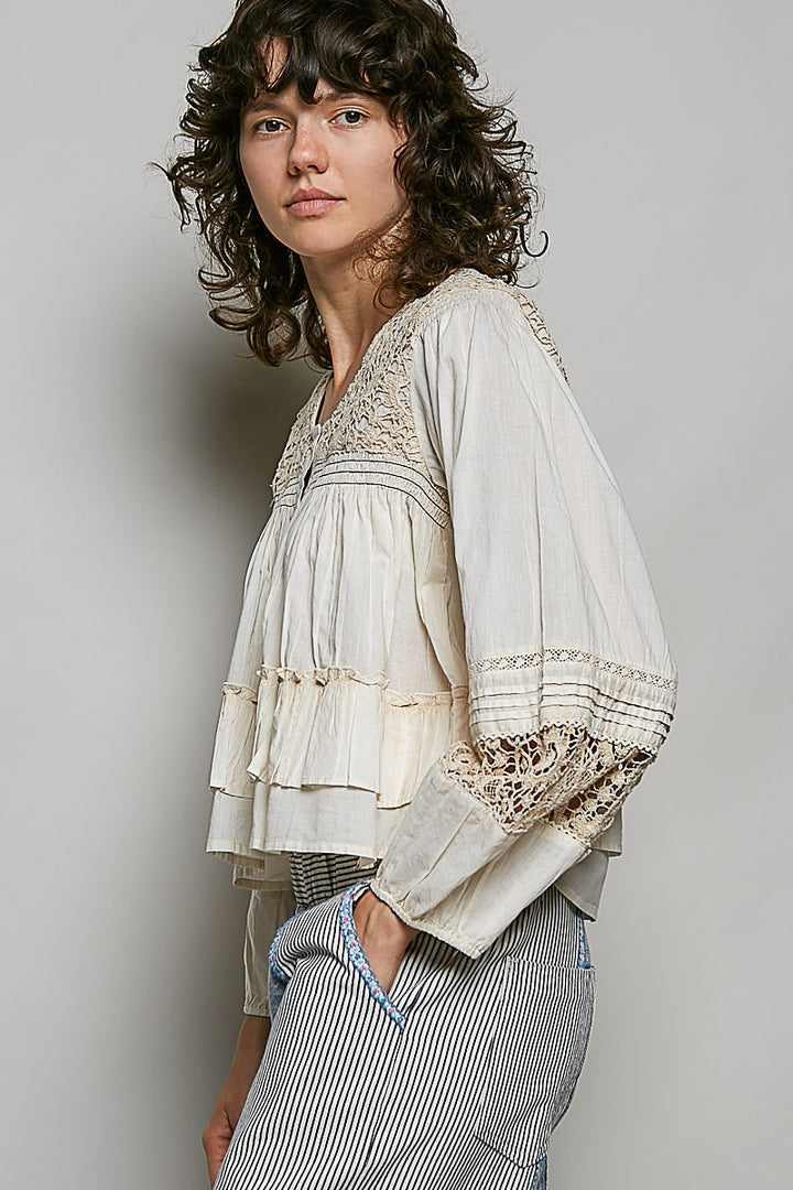 Person wearing a light-colored blouse with lace details on a plain background