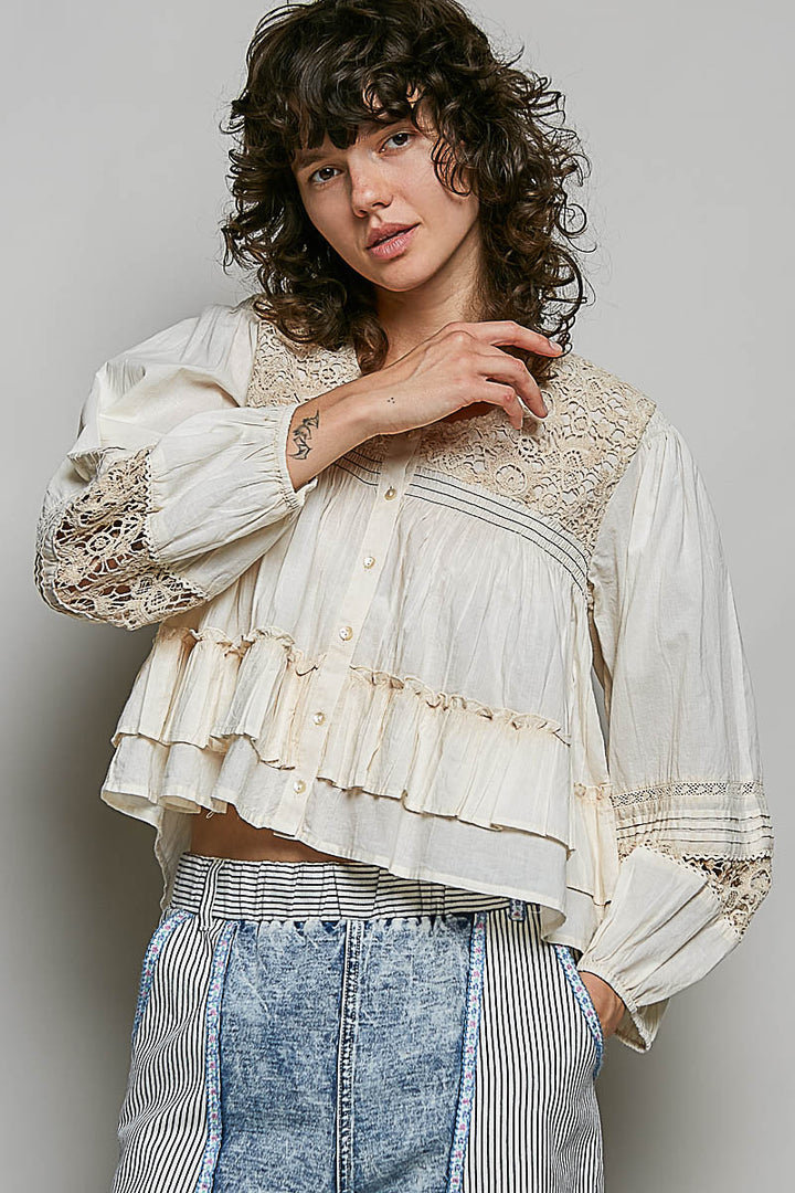 Woman wearing a white lace blouse with long sleeves and blue jeans against a plain background
