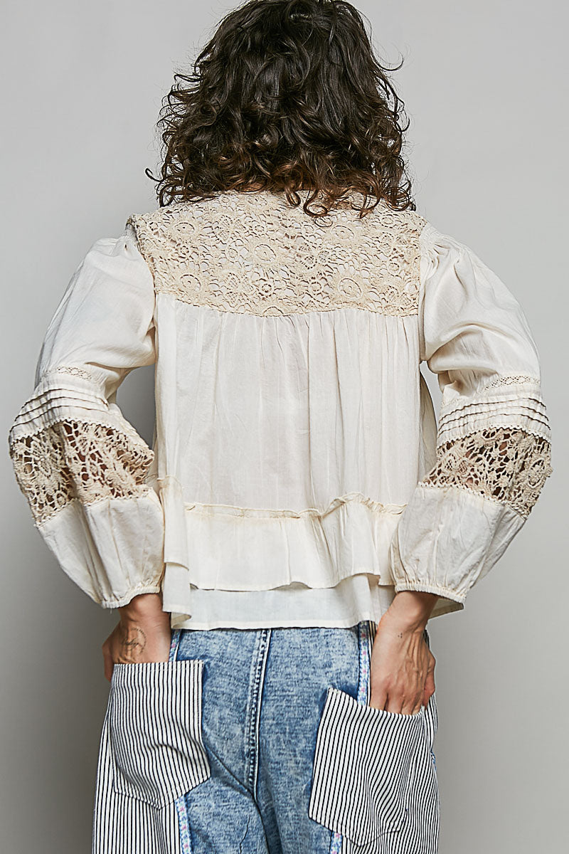 Person wearing a white blouse with lace details on a plain background