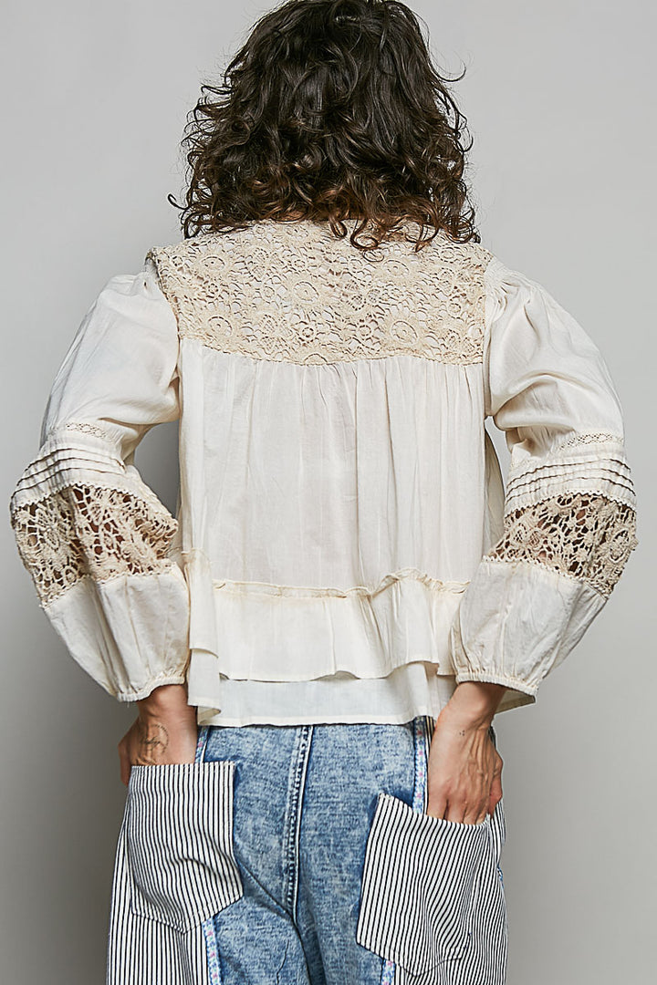 Person wearing a white blouse with lace details on a plain background