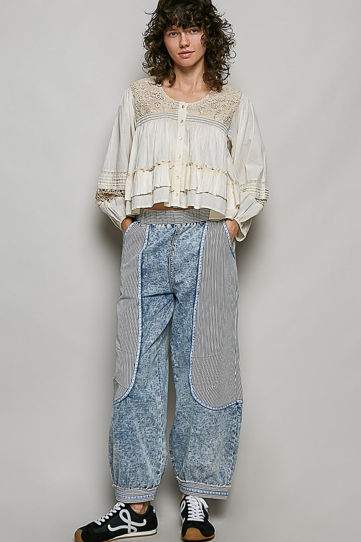 Person wearing a layered outfit with a white top and blue acid-wash pants against a plain background
