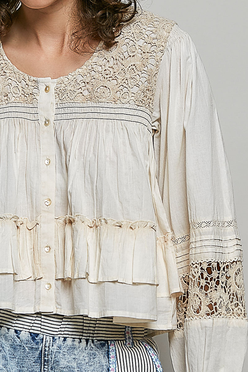 Close-up of a woman wearing a lace-trimmed blouse with a neutral background