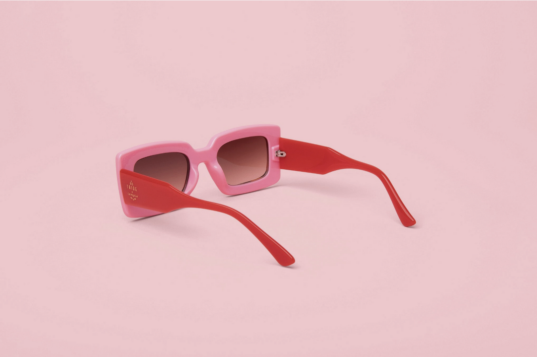 Pink and red cat-eye sunglasses with gradient brown lenses, displayed on a solid light pink background.