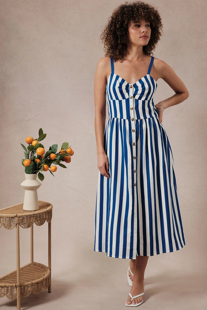 Woman wearing a blue and white striped dress standing next to a small table with a floral arrangement.