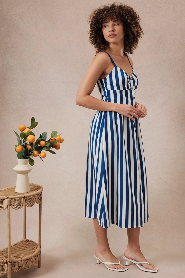 Woman wearing a blue and white striped dress standing next to a small table with a plant on a beige background