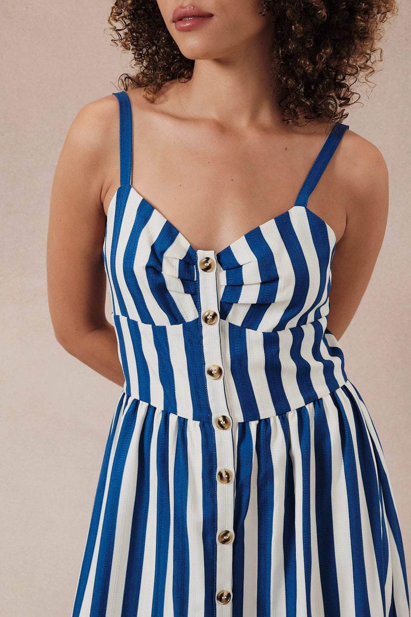 Woman wearing a blue and white striped dress with gold buttons on a beige background