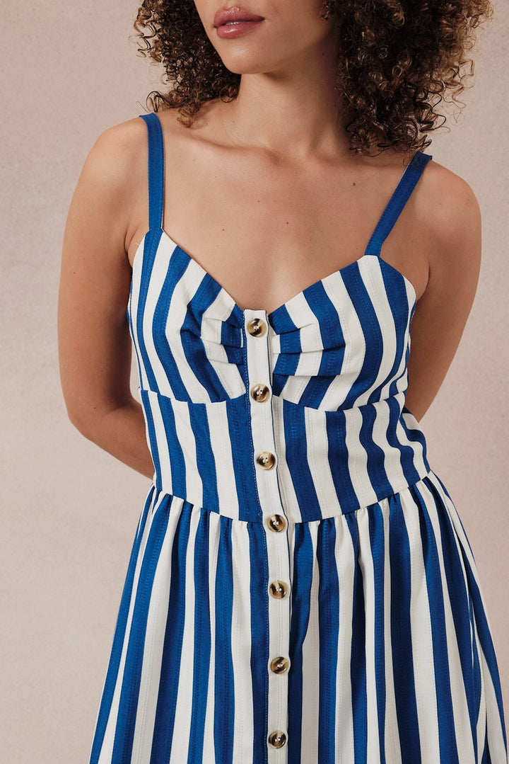 Woman wearing a blue and white striped dress with gold buttons on a beige background