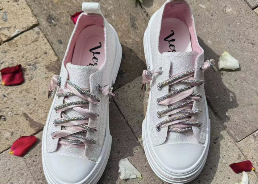 White glitter sneakers with sparkle and pink ribbon laces on sidewalk with rose petals