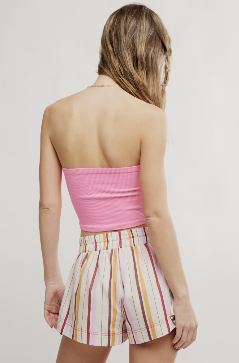 Woman wearing a pink strapless top and striped shorts on a plain background